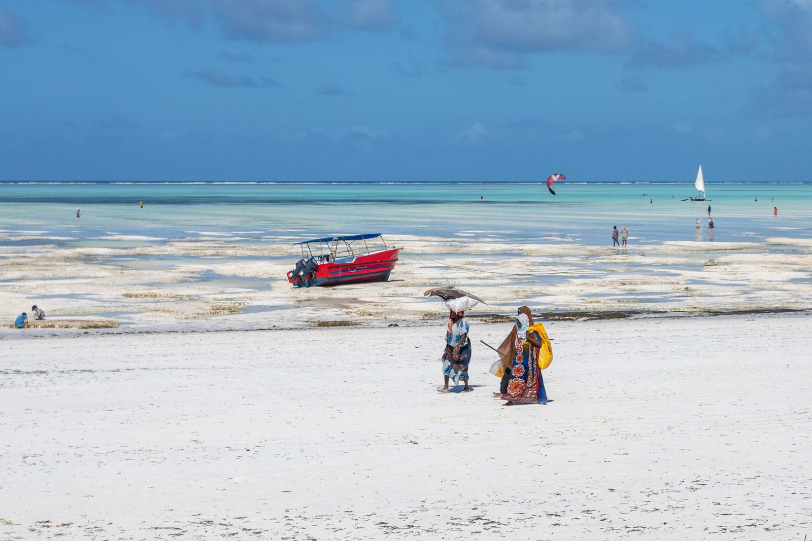 Women walking on an African beach beside a vibrant red boat